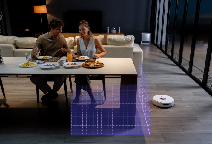 Narwal Freo Z Ultra robot vacuum working under the dining table while two people are seated, enjoying a meal.